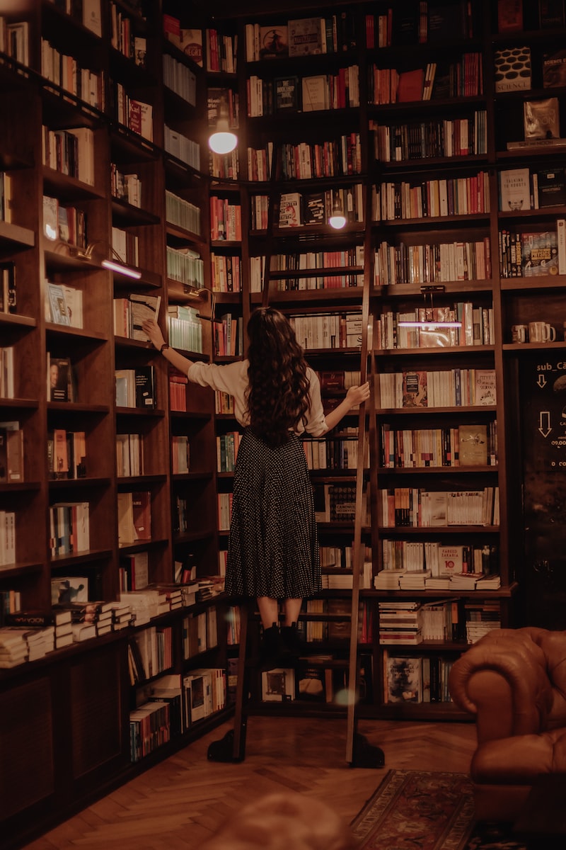 woman in black dress standing in front of books